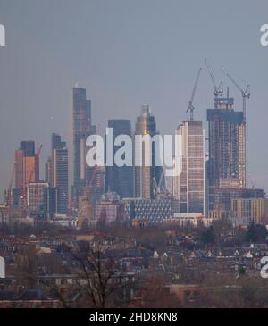 London, Großbritannien. 4. Januar 2022. Sinkende Temperaturen und strahlender Himmel über dem Zentrum Londons, wenn die untergehende Sonne die hohen Bürohochhäuser der City of London trifft, von Wimbledon aus gesehen über Vorstadthäusern im Vordergrund. Quelle: Malcolm Park/Alamy Live News Stockfoto