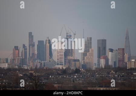 London, Großbritannien. 4. Januar 2022. Sinkende Temperaturen und strahlender Himmel über dem Zentrum Londons, wenn die untergehende Sonne die hohen Bürohochhäuser der City of London trifft, von Wimbledon aus gesehen über Vorstadthäusern im Vordergrund. Quelle: Malcolm Park/Alamy Live News Stockfoto