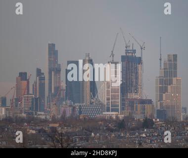 London, Großbritannien. 4. Januar 2022. Sinkende Temperaturen und strahlender Himmel über dem Zentrum Londons, wenn die untergehende Sonne die hohen Bürohochhäuser der City of London trifft, von Wimbledon aus gesehen über Vorstadthäusern im Vordergrund. Quelle: Malcolm Park/Alamy Live News Stockfoto