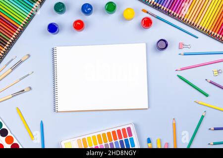 Kreative Kunstwerke liefern Hintergrund. Aquarell, Pinsel, Bleistifte, offenes leeres Notizbuch auf blauem Tisch. Draufsicht, flach liegend Stockfoto