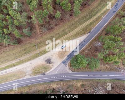 Die Kreuzung von Asphalt- und Forststraßen in einem dichten Wald im Herbst von oben gesehen. Tag. Stockfoto