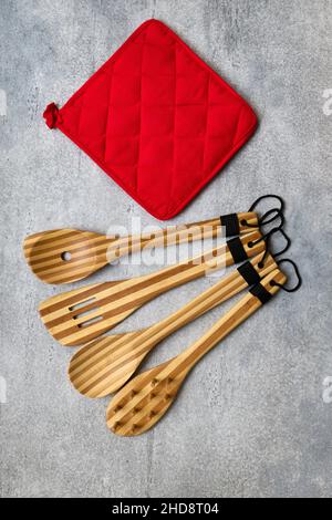 Küchengeräte aus Bambus aus Holz und roter Ofenhandschuh auf grauem Betongrund Stockfoto