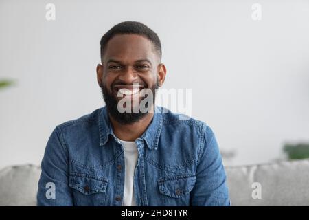 Porträt von fröhlichen jungen attraktiven afroamerikanischen Männchen mit Bart Blick auf die Kamera im Innenraum Stockfoto