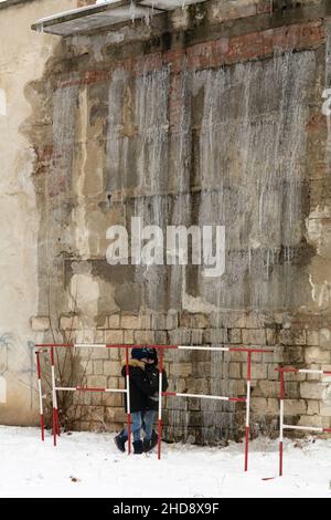 Tiraspol, Moldawien - 31. Dezember 2021: Kinder ohne elterliche Aufsicht befinden sich in der Gefahrenzone unter großen hängenden Eiszapfen. Stockfoto