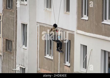 Tiraspol, Moldawien - 19. November 2021 Hochhaus. Blick auf einen Arbeiter, der eine Wand eines Mehrfamilienhauses klettert, um Fensterhänge zu beenden Stockfoto