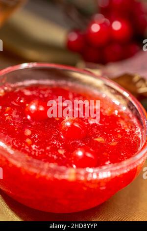 Viburnum Marmelade in einer Glasschale auf dem rustikalen Holztisch mit einem heißen Wintergetränk und Viburnum-Beeren Stockfoto