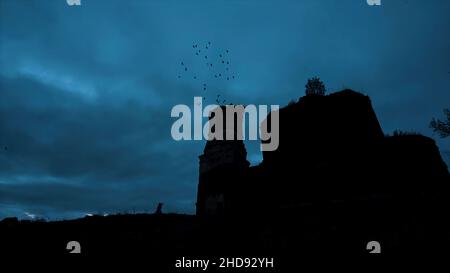 Mystische Silhouette eines Tempels oder einer Burg gegen den bewölkten Himmel und Raben, die nachts am Himmel fliegen. Video. Das große alte Steinschloss auf dem Rock du Stockfoto