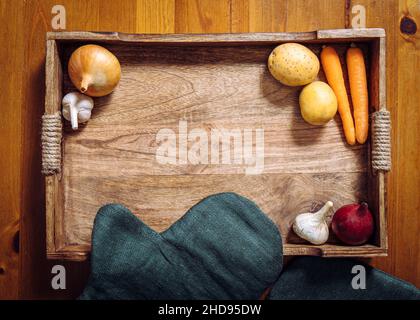 Flache Ansicht von verschiedenen Wurzelgemüse auf Holztablett auf Küchentisch. Viel Platz für Kopien in der Mitte. Karotten, Knoblauch, Zwiebeln, Kartoffeln. Stockfoto