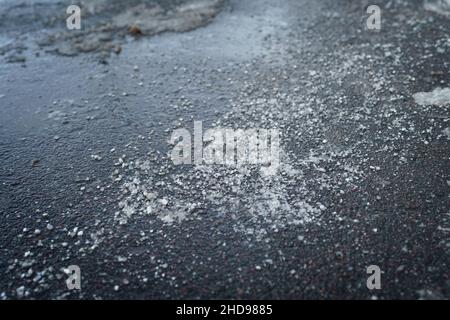 Enteisungsreagenz im Winter auf der Straße. Der Bürgersteig ist mit technischem Salz bestreut Stockfoto