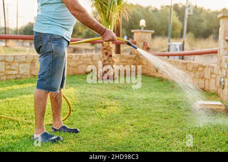 Mann, der den Rasen am Morgen mit einem Schlauch wässert Stockfoto