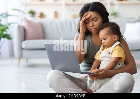 Müde Schwarze Mutter Mit Problemen Mit Remote-Arbeit, Während Babysitting Kleinkind Kind Stockfoto