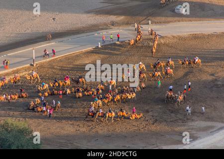 DUNHUANG, CHINA - 21. AUGUST 2018: Touristen reiten auf Kamelen in der Singing Sands Dune in der Nähe von Dunhuang, Provinz Gansu, China Stockfoto