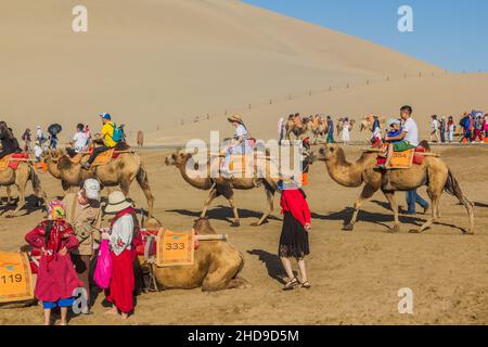 DUNHUANG, CHINA - 21. AUGUST 2018: Touristen reiten auf Kamelen in der Singing Sands Dune in der Nähe von Dunhuang, Provinz Gansu, China Stockfoto