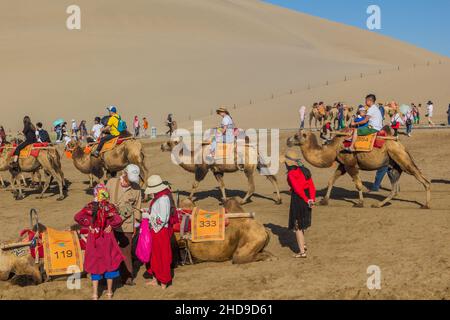 DUNHUANG, CHINA - 21. AUGUST 2018: Touristen reiten auf Kamelen in der Singing Sands Dune in der Nähe von Dunhuang, Provinz Gansu, China Stockfoto