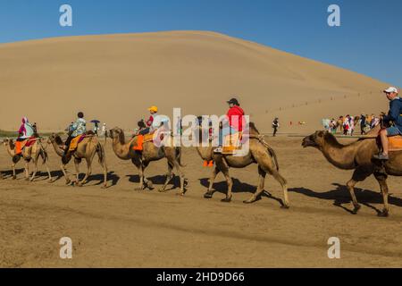 DUNHUANG, CHINA - 21. AUGUST 2018: Touristen reiten auf Kamelen in der Singing Sands Dune in der Nähe von Dunhuang, Provinz Gansu, China Stockfoto