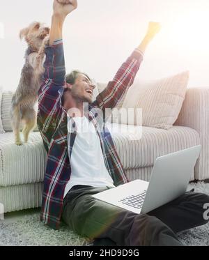 Happy Guy frohlockt mit seinem Hund sitzt in der Nähe der Couch im Wohnzimmer. Stockfoto