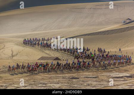 DUNHUANG, CHINA - 21. AUGUST 2018: Touristen reiten auf Kamelen in der Singing Sands Dune in der Nähe von Dunhuang, Provinz Gansu, China Stockfoto