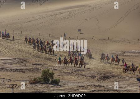 DUNHUANG, CHINA - 21. AUGUST 2018: Touristen reiten auf Kamelen in der Singing Sands Dune in der Nähe von Dunhuang, Provinz Gansu, China Stockfoto