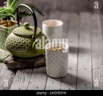 Stillleben einer Tasse Tee mit einer Schachtel Kräutertee und einer traditionellen Teedose aus grünem Metall im Hintergrund. Stockfoto