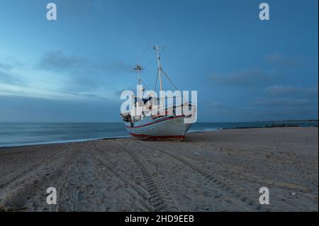 Einsames Fischerboot am Sandstrand bei ruhigem Wetter nach dem Sonnenuntergang in Thisted, Dänemark Stockfoto