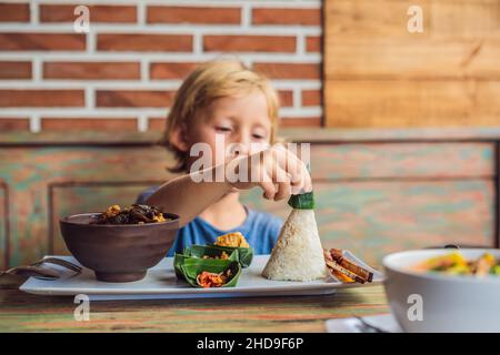 Junge isst in einem Café. Lifestyle. Ein Gericht bestehend aus Reis, gebratenem Fisch mit Holzpilzen und verschiedenen Saucen Stockfoto