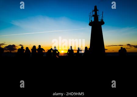 Silhouette einer mittleren Gruppe von Menschen, die den Sonnenuntergang vom Leuchtturm Ponta do Humatia in Salvador, Bahi, genießen Stockfoto