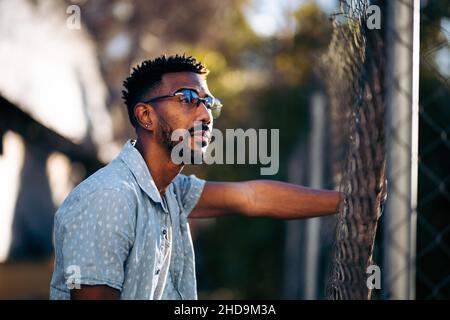 Hübscher afroamerikanischer Mann, der sich nachdenklich auf einen Zaun stützt Stockfoto