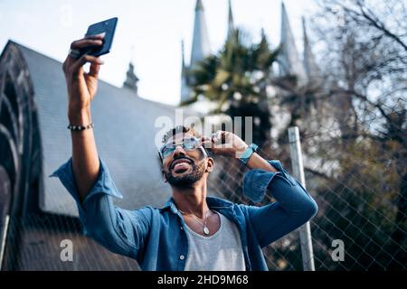 Stilvoller Afro-Mann mit Brille beim Selfie mit seinem Smartphone auf der Straße Stockfoto