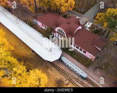 Children's Southern Railway Station. Gleislinie und Bahnsteig mit Zug im leuchtend gelben Herbstpark. Luftkiefenansicht auf buntem Kharkiv, Reise U Stockfoto