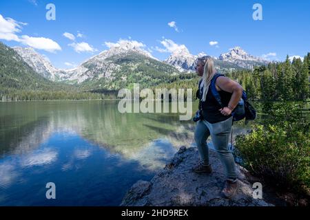 Besorgte blonde Wandererin steht auf einem Felsen am Ufer des Taggart Lake im Grand Teton National Park Stockfoto