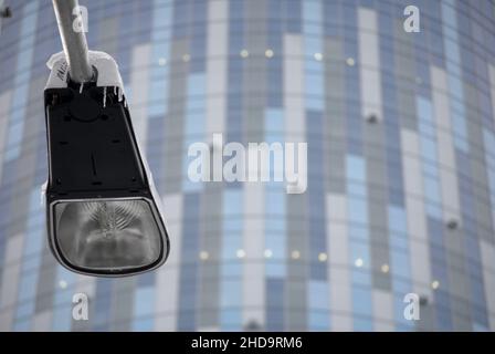 Nahaufnahme eines Laternenpfostens mit Eiszapfen, abgebildet mit einem modernen Bürogebäude im Hintergrund. Stockfoto