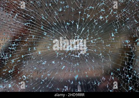 Kaputtes Autofenster mit gebrochenem Glasmuster und einem Einschussloch in der Mitte. Stockfoto