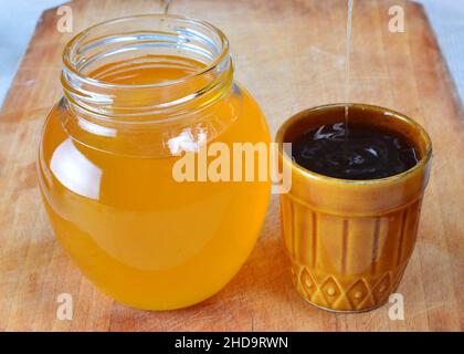 Frischer natürlicher Bio-Honig, der in einer kleinen rustikalen Tasse neben einem Glas voller Honig gegossen wird. Stockfoto