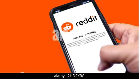 Rom, Italien, Januar 2022: Hand hält ein Smartphone mit der mobilen Reddit-App auf dem Bildschirm auf einem orangefarbenen Hintergrund. Reddit ist eine amerikanische Social News Stockfoto