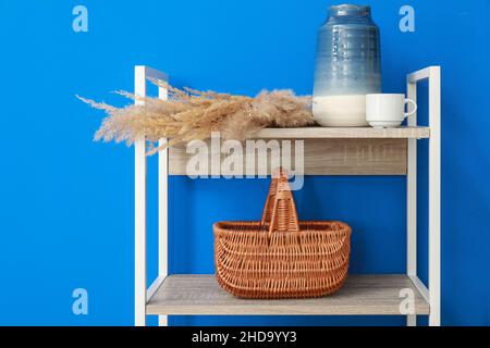 Regal mit Vase, Pampagras, Tasse und Korb an der blauen Wand Stockfoto