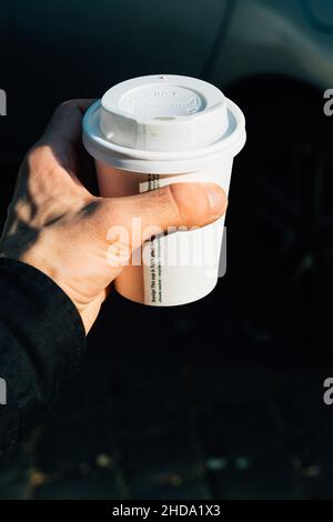 Nahaufnahme einer Hand mit einer weißen Tasse Kaffee zum Mitnehmen am Morgen Stockfoto