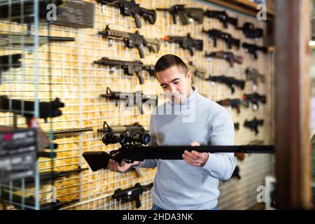 Erwachsene Mann wählt Gewehr mit Teleskopausblick und Schalldämpfer Stockfoto