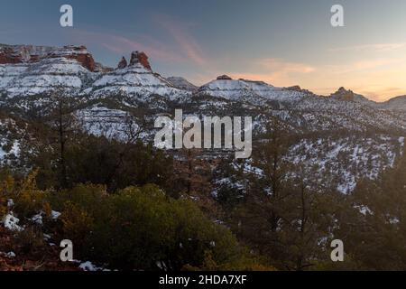 Ein farbenfroher Sonnenuntergang erhellt den Himmel über einer zerklüfteten Landschaft des Sedona und des Oak Creek Canyon an der Mündung des Wilson Canyon nach einem kürzlichen Wintersturm Stockfoto