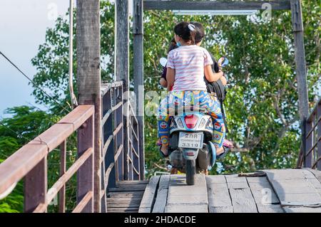 Motorrad mit drei Personen, die eine Holzbrücke über einen Kanal in Bangsaothong, Provinz Samut Prakan in Thailand, überqueren. Stockfoto