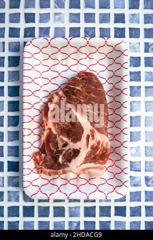 Frisches Schweinefleisch im Verpackungstablett auf blauem Fliesentisch. Draufsicht Stockfoto
