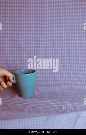 Hand hält eine Tasse Kaffee auf violettem Karomuster Stoff Hintergrund Stockfoto