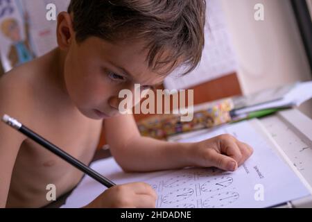 Während der pandemischen Schulsperre arbeitet ein kleiner Junge von zu Hause aus an der Schule Stockfoto