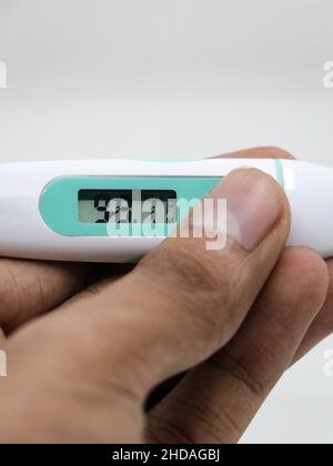 Eine Nahaufnahme des niedrigen Messwerts in einem Digitalthermometer in den Händen einer Person, die auf weißem Hintergrund isoliert ist Stockfoto