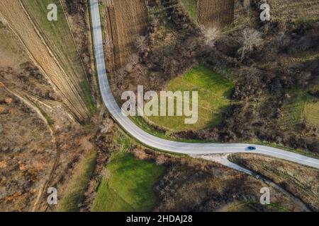 Luftaufnahme von oben auf der Landstraße in der Bergkette zwischen Feldern Gras und Bäumen ringsum - Naturreisekonzept Drohne Foto auf Stockfoto