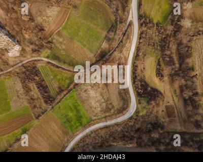 Luftaufnahme von oben auf der Landstraße in der Bergkette zwischen Feldern Gras und Bäumen ringsum - Naturreisekonzept Drohne Foto auf Stockfoto