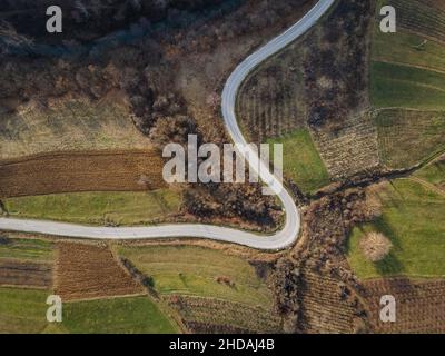 Luftaufnahme von oben auf der Landstraße in der Bergkette zwischen Feldern Gras und Bäumen ringsum - Naturreisekonzept Drohne Foto auf Stockfoto