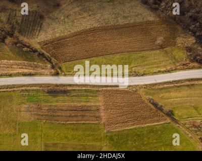 Luftaufnahme von oben auf der Landstraße in der Bergkette zwischen Feldern Gras und Bäumen ringsum - Naturreisekonzept Drohne Foto auf Stockfoto