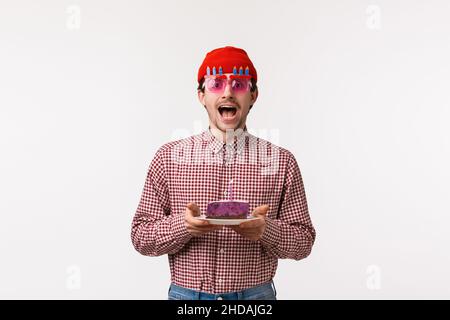 Celebration, Urlaub und Lifestyle-Konzept. Aufgeregt fröhlicher, gutaussehender erwachsener Kerl, der Geburtstag mit Freunden in lustigen Gläsern feiert und b hält Stockfoto