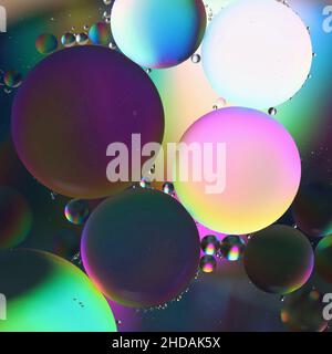 Öl tropft auf eine Wasseroberfläche, reflektiert farblich gefärbtes Licht, abstrakter Hintergrund Stockfoto
