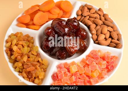 Mischung aus getrockneten Früchten und Nüssen auf einem weißen Teller. Aprikose, Mandel, Rosinen, Datteln Frucht. Auf einem beigen Hintergrund. Platz für Text oder Design. Stockfoto